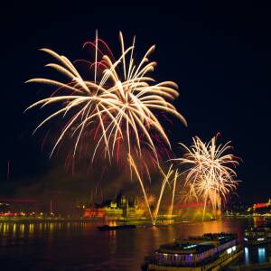 fireworks over the danube in budapest, seen from the margidhíd (margaret bridge), ships in the foreground, parliament in the middle, behind the fireworks, and the castle to the right